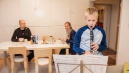 perhe istuu keittiössä ja poika soittaa klarinettia