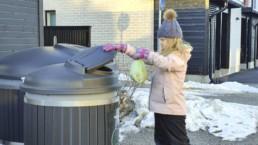 Tyttö laittaa roskapussia keräysastiaan talvella.